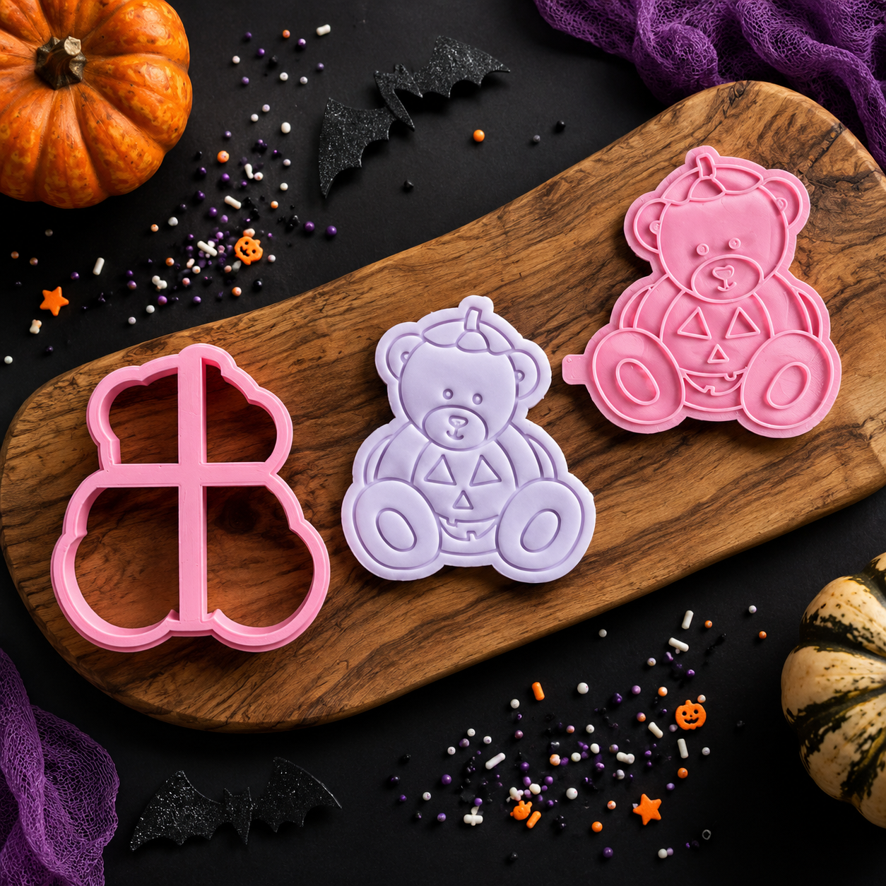 Three Halloween-themed cookie cutters on a wooden board with pumpkins and sprinkles around.