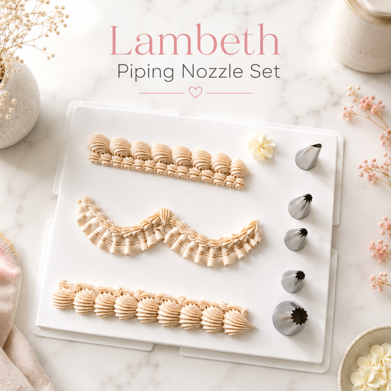 Lambeth Piping Nozzle Set displayed on a white tray over a marble surface, with decorative flowers and a small bowl around it. The set includes several beige and silver piping tips arranged on a clear plastic case, with the text 'Lambeth Piping Nozzle Set' above.

