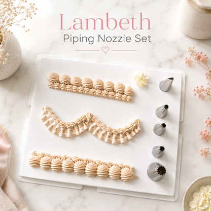 Lambeth Piping Nozzle Set displayed on a white tray over a marble surface, with decorative flowers and a small bowl around it. The set includes several beige and silver piping tips arranged on a clear plastic case, with the text 'Lambeth Piping Nozzle Set' above.

