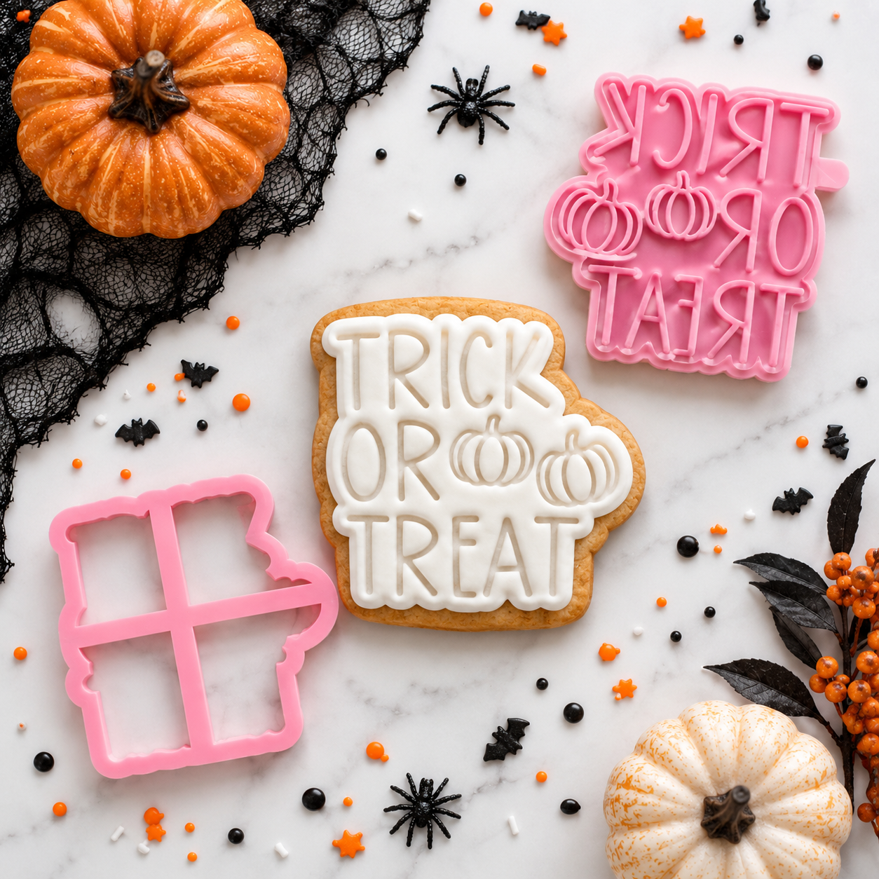 Halloween-themed cookie with 'Trick or Treat' text, surrounded by cookie cutters and decorative elements on a marble surface.