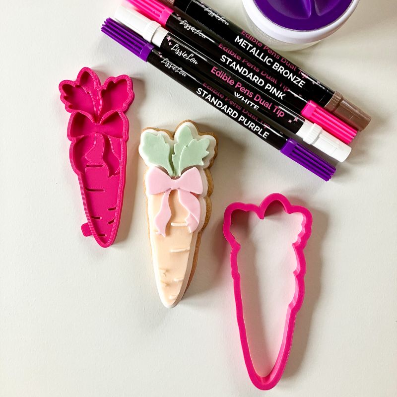 Carrot-shaped cookie cutters and edible pen markers on a white surface